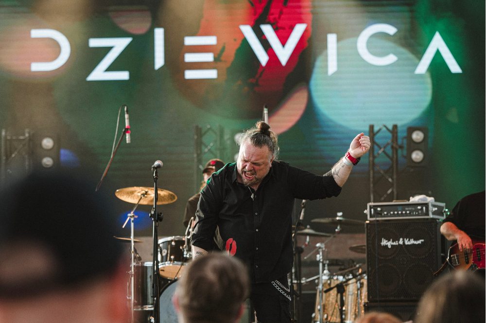 Wokalista Dziewicy podczas koncertu, w tle logo zespołu
